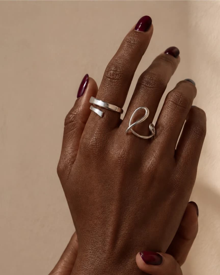 Mãos com anéis prateados e unhas em tom vinho.